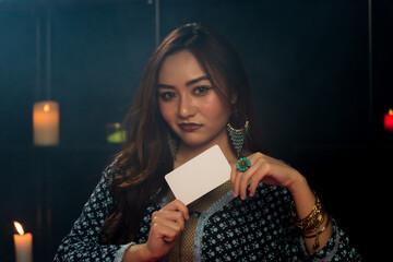 Naklejka premium Portrait of Asian beautiful Gypsy fortune teller woman in dark room with white tarot card