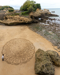 talented street artist draws mandala in the sand at the beach in Biarritz