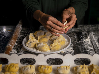 Female hands sculpt dumplings with meat over the kitchen table. Close-up of the hands of an adult woman with a slice of minced meat and dough. The process of making homemade meat dumplings. Homemade