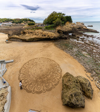 talented street artist draws mandala in the sand at the beach in Biarritz
