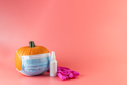Natural organic pumpkin vegetable in protective medical face mask with sanitizer gel  and pink gloves on a peach color background with soft shadow, copy space. Halloween celebration under quarantine