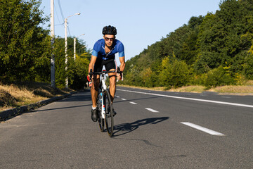 A person riding a bike. Road bike race near the forest. Sports activity. Professional cyclist on a road. 