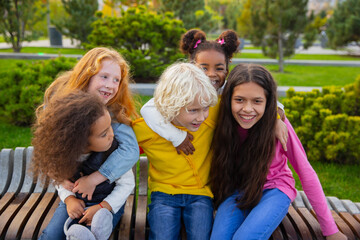 Fototapeta premium Moments. Interracial group of kids, girls and boys playing together at the park in summer day. Friendship has no race. Happiness, childhood, education, diversity concept. Look happy and sincere.