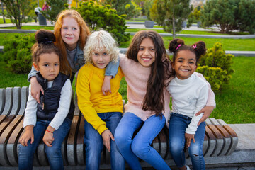 Fototapeta premium Warm. Interracial group of kids, girls and boys playing together at the park in summer day. Friendship has no race. Happiness, childhood, education, diversity concept. Look happy and sincere.
