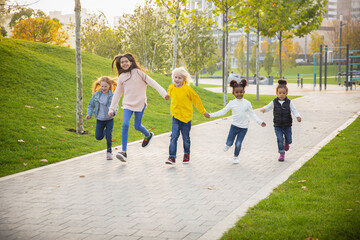 Fototapeta premium Running. Interracial group of kids, girls and boys playing together at the park in summer day. Friendship has no race. Happiness, childhood, education, diversity concept. Look happy and sincere.