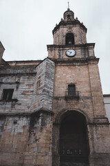 Fototapeta na wymiar Medieval church with clock and bell in Portugalete, Spain. Religious architecture. Ancient cathedral tower with outdoor clock on facade. Elegant catholic church. Old stone church. with closed entrance