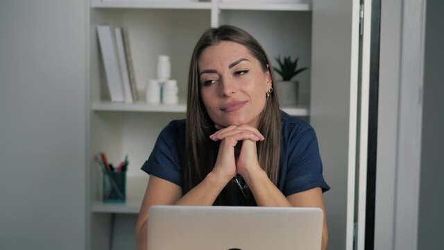 attractive femake doctor practitioner in dark-blue coat sitting at workplace, thinking of problem solution or medical advice while consulting patient online by healthcare application on computer. 4k