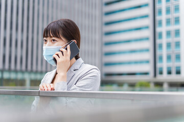 Fototapeta premium マスクをして電話をする若いビジネスウーマン