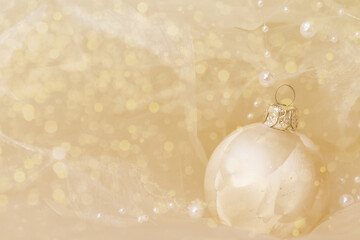 golden christmas ball on golden background with pearls and silk and glitter bokeh, focus on the right side