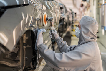 An employee of the car body paint shop with a medical mask on his face polishes the painted surface