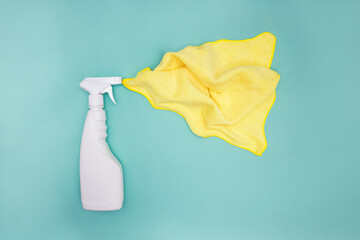 White spray plastic bottle of cleaner on green background with yellow cloth.