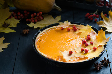 Traditional homemade pumpkin tart pie decorated with autumn leaves on dark wooden background, selective focus. Halloween or thanksgiving holiday celebration meal.