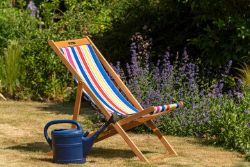 England UK. June 2020, An open colourful deckchair in an English country garden with a watering can