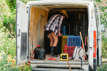 Young farmer woman looking inside a van with hoe