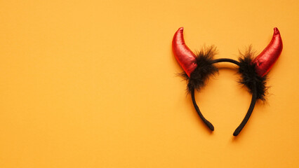 Red devil horns head hoop on orang background. Accessory for Halloween celebration, top view, flat lay, copy space © Komchatnykh Tetiana
