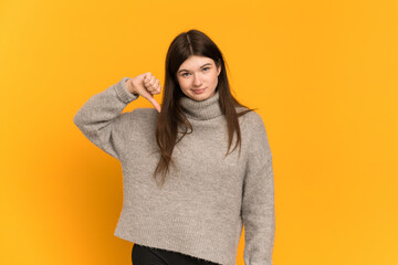 Young Ukrainian girl isolated on yellow background showing thumb down with negative expression