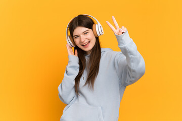 Young Ukrainian girl isolated on yellow background listening music and singing