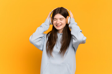 Young Ukrainian girl isolated on yellow background listening music