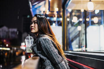 beautiful young lonely asian girl standing outside a cafe or restaurant, on a street night, it's raining, she is waiting for a bus or someone meets.