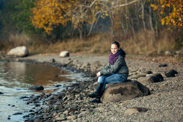 Teen girl sits on a rock on the Bank of the river.