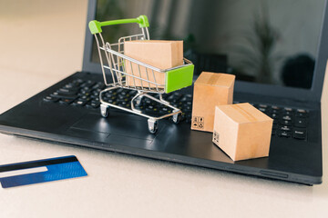 Close-up of a shopping cart with a box, next to a laptop and credit card, on the desk.