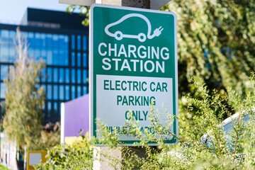 Electric car road sign charging station. Outdoor car parking and charging point for electric vehicle. Electric car charging station sign in front of public parking lot