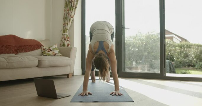 Female practicing yoga exercise at home watching video tutorial on laptop