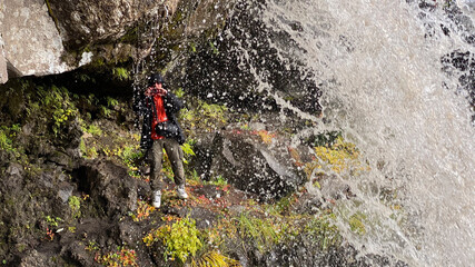 A photographer stands under a beautiful waterfall and takes pictures.