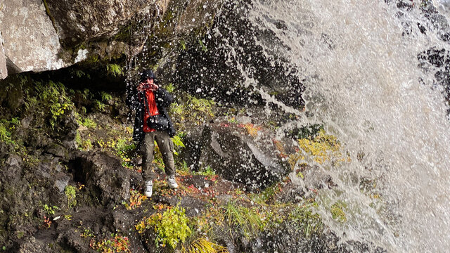 A photographer stands under a beautiful waterfall and takes pictures.