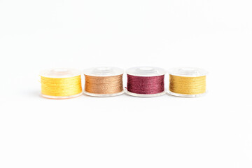 Different spools of mixed beige, yellow and brown cotton thread prepared for sewing machine, isolated on white, side view.