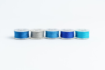 One line of mixed colourful blue spools of cotton thread displayed horizontally, isolated on white, top view.