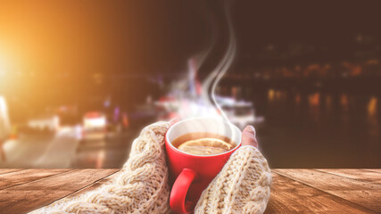 Autumn background, hot cup of tea. Red cup in female hands on the background of the autumn landscape. Sunlight, wooden table in nature.