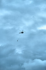 Fototapeta na wymiar Fire fighting helicopter with water bucket on a gloomy sky background