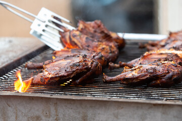 Chicken halves grilling on large commercial rotisserie. Meat being roasted on grates and flames for large barbeque gathering. 