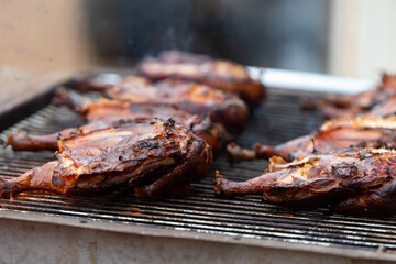 Chicken halves grilling on large commercial rotisserie. Meat being roasted on grates and flames for large barbeque gathering. 