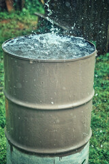 Naklejka na ściany i meble Rain barrel. Strong stream of water pours into an old metal barrel during heavy rain