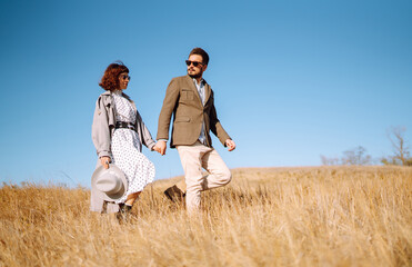 Stylish  young couple enjoying autumn weather in autumn field. Lovely couple walking and hugging in the field together. The concept of youth, love and lifestyle.