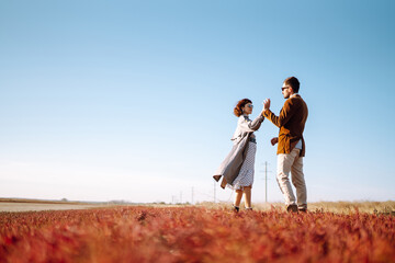 Young loving couple walking and hugging in autumn field. Enjoying time together. Fashion, lifestyle and autumn mood.