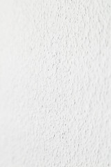 Vertical uniform white roughly textured wall with selective focus