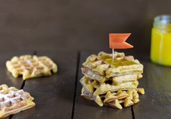 Carrot waffles with honey on a brown wooden background.