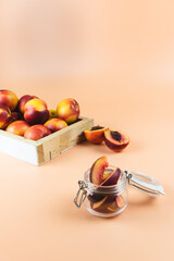 Little glass jar full of cut peaches, nectarines, Red very ripe peaches inside a wooden box for sale in the back. Peachy colored background