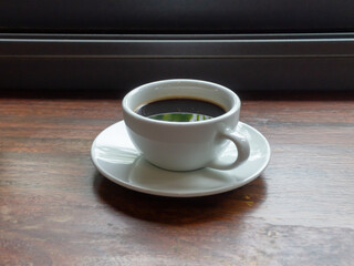 White coffee cup with black coffee placed on the wooden table