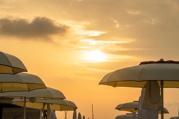 Naklejka na ściany i meble Sunset at the beach with beach umbrellas and orange sky
