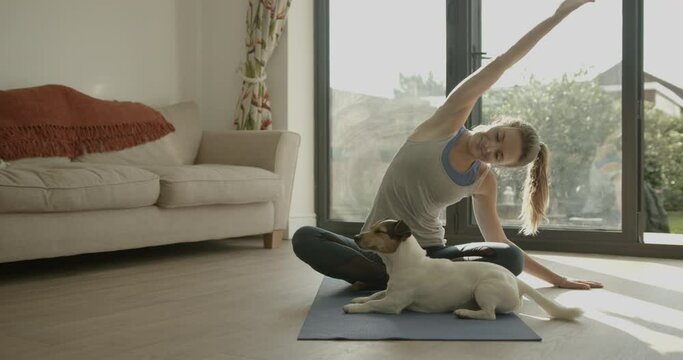Female practicing yoga exercise at home together with dog on floor