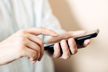 Female hands are holding a black phone, pressing a smartphone with a finger, touching.