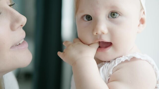 New parent with their baby. little girl and her mom close up. A cute baby in a beautiful bow on his head smiles at mom. Young mother kissing daughter