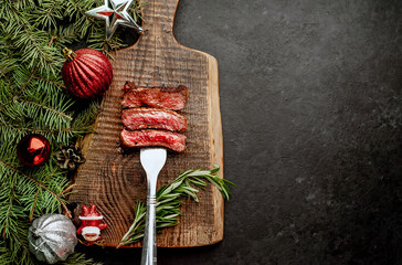 Different degrees of roasting of steak on a meat fork for Christmas on a background of a stone with a spruce and Christmas toys with copy space for your text