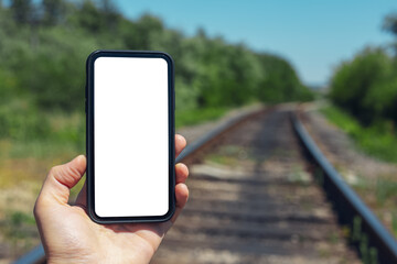 Fototapeta na wymiar Close-up of male hand holding smartphone with mockup background of blurred railway.