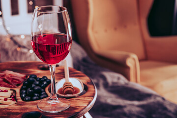  A glass of red wine and a snack on a tray in the bedroom. Rest in a cozy home. Selective focus, free space for text. Toned photo