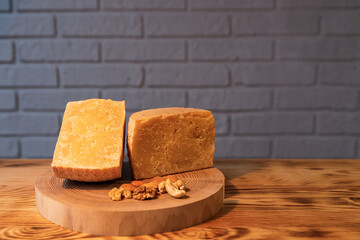 A head of aged cheese cut in half on a wooden Board with various nuts on the background of a brick wall
